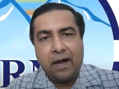 Sanjeeb Sapkota is speaking in a video call with NRNA logo in the background.